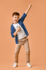 Cute little boy dancing and listening to music against color background