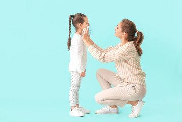 Mother wearing protective mask onto face of her little daughter against color background