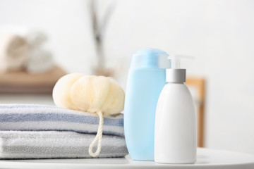 Fototapeta na wymiar Different shower gels, towel and loofah on table in bathroom