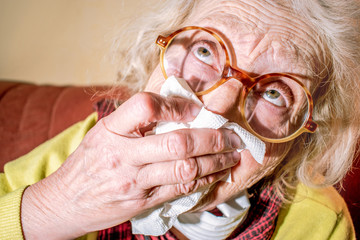 Funny older wrinkled woman in a protects mask and glasses with a handkerchief at home. Older people with symptoms of coronovirus COVID-2019. Senior Health. Insulation. Quarantine Paranoia and Fear