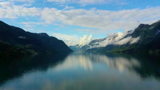 Aerial drone flight over water in the Hardangerfjord fjord, Norway. An oblong bay surrounded by green mountains with fog on the hillside. Shot in the summer at sunset