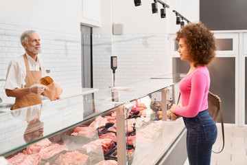 Lady choosing raw meat behind counter.