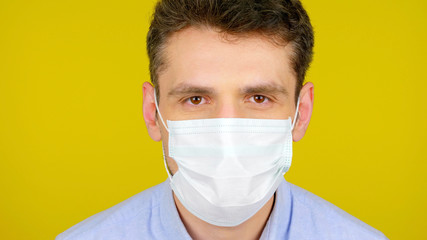 Closeup man in protective medical mask looks at the camera. Head on a yellow background. Concept against the virus: Coronavirus, flu
