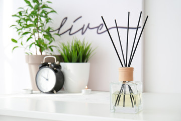 Reed diffuser, clock and houseplants on table in room