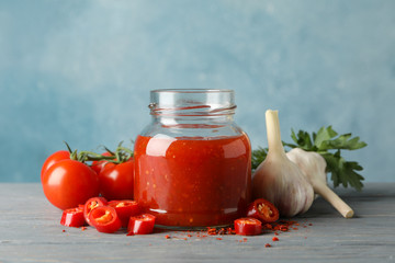 Jar with red chilli and tomato sauce, and spices on wooden table