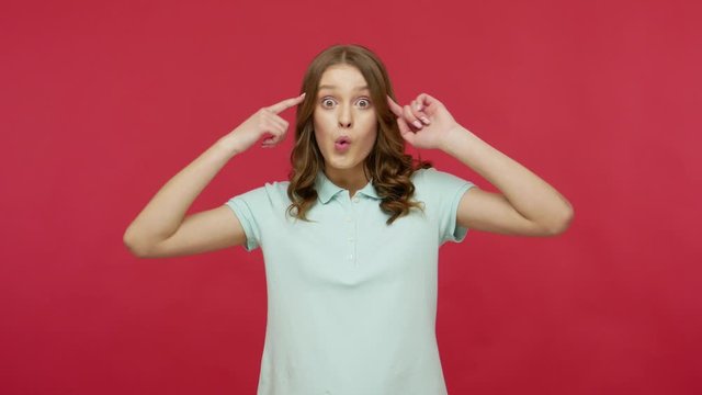 You are crazy, out of mind! Young brunette woman in polo t-shirt making stupid gesture with finger near head, looking annoyed and blaming for insane idea. indoor studio shot isolated on red background