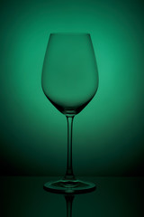 The crystal glass stands on the reflecting surface on a green background. studio photo. product. Beautiful shadow from wine glass. macro photo