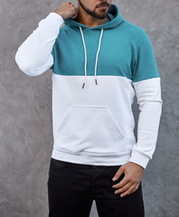 young man in white and torqouise hoodie standing outdoors on gray background