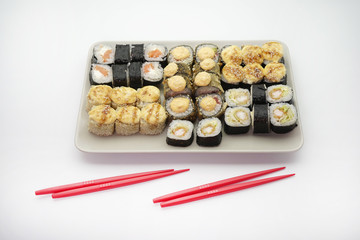 Rectangular plate full of hand-rolled sushi, sushi set, and red chopsticks, close-up.