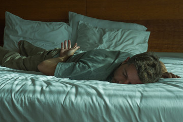 lifestyle portrait of young attractive tired and exhausted man lying down on bed sleeping during the day with sunlight filtering in the bedroom