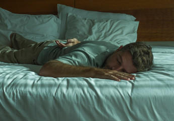 lifestyle portrait of young attractive tired and exhausted man lying down on bed sleeping during the day with sunlight filtering in the bedroom