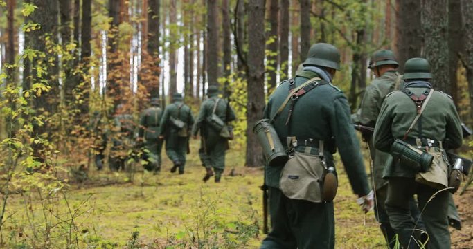 Historical Re-enactment. Re-enactors Dressed German Wehrmacht Infantry Soldiers In World War II Marching Along Forest In Autumn Day. Group of Soldiers Marching In Forest