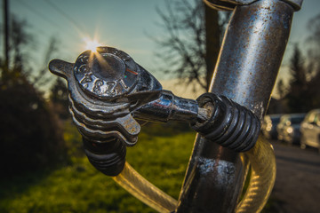 Detail of cheap worn number combination lock on an old bicycle, with sun streak or flare just behind the lock. Park setting or outside in suburb of a city