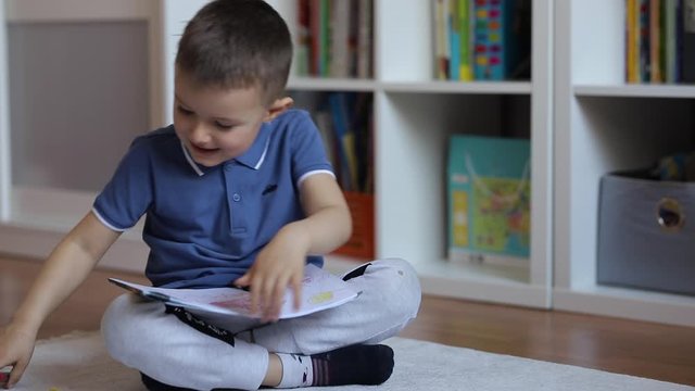 The child draws in an album sitting on the floor in the room