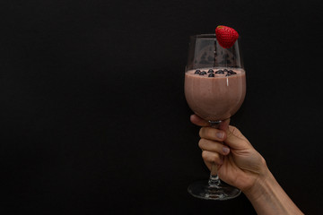 The girl holds in her hand a natural cocktail in a wine glass, with one strawberry on top. Black background. Horizontal view. Close-up. Copy space