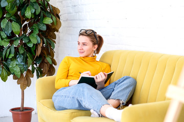 girl works at home sitting on a yellow sofa