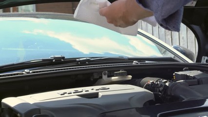 Man checking oil level in car blue shirt paper towel