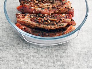 Pork belly slices marinated in soy sauce and herbs in a glass bowl on a light table cloth.