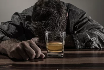 Fotobehang young messy and drunk alcohol addict man drinking whiskey glass at home sitting thoughtful and depressed as alcoholic suffering alcoholism problem and addiction © TheVisualsYouNeed