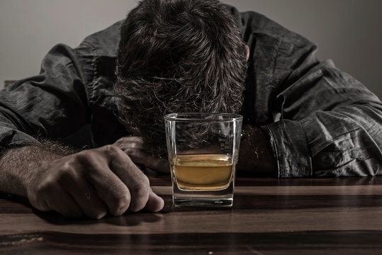 young messy and drunk alcohol addict man drinking whiskey glass at home sitting thoughtful and depressed as alcoholic suffering alcoholism problem and addiction