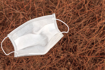 a single piece of a protective disposable surgical face mask left and lying on a bush