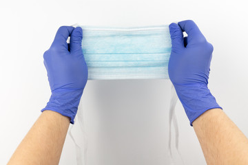 Hands with protective gloves holding a blue disposable face mask
