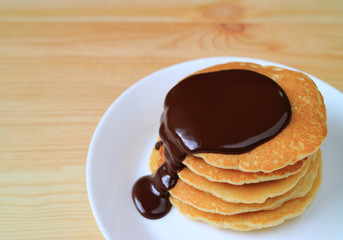 Stack of homemade pancakes with melting dark chocolate sauce served on wooden table