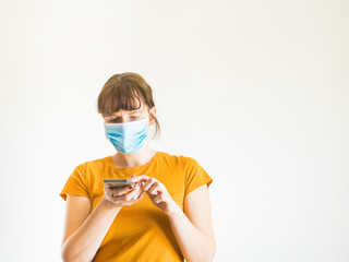 Young caucasian woman in yellow T-shirt wearing protective face mask using smartphone