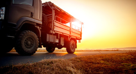 military truck running on asphalt highway against beautiful sunset sky