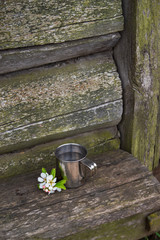 An iron Cup of water on a bench, against the wall of an old wooden house.