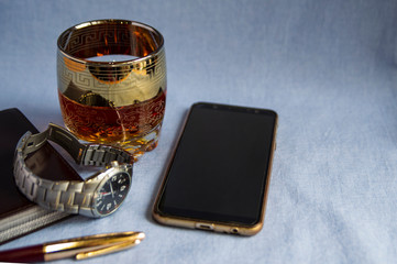Whiskey in a glass on the wooden table. Men's watch, notebook, and cell phone.