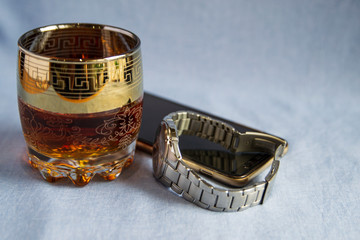 Whiskey in a glass on the wooden table. Men's watch, notebook, and cell phone.