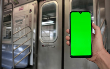 Close up of man hand holding smartphone with green mock up screen inside underground metro train