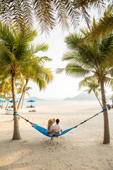 a couple loving hug each other while seating on a hammock at the beach