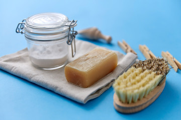 cleaning stuff, sustainability and eco living concept - natural brush, washing soda in glass jar and laundry soap on canvas with wooden scoop and clothespins on blue background