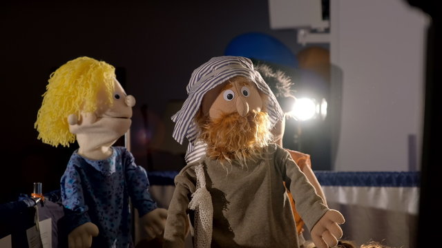 Three puppet dolls hiding under the scenes during the performance in puppet theater. Two puppet men with beard and in typical Asian clothing