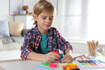 Little boy playing with plasticine at table indoors. Creative hobby