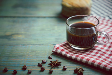 Americano coffee in clear coffee cup put on red scottish pattern fabric with coffee beans and fresh bread on old wooden table background.With copy space and selective focus.