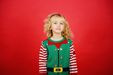 Little girl in Santa elf helper costume on bright red vivid color background.
