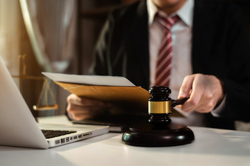 Justice and law concept. Male judge in a courtroom the gavel, working with digital tablet computer on wood table in sun light.