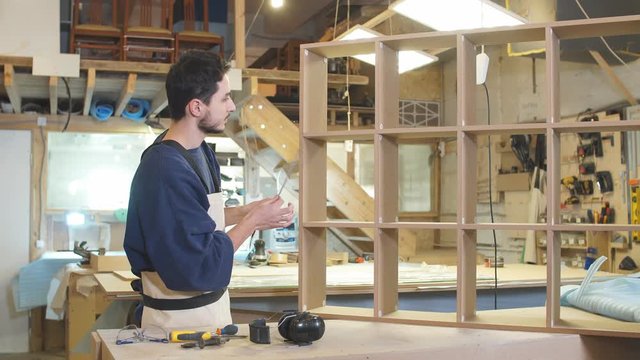 Confident furniture maker measures handmade wooden shelf, carpenter made construction on an order for customers.