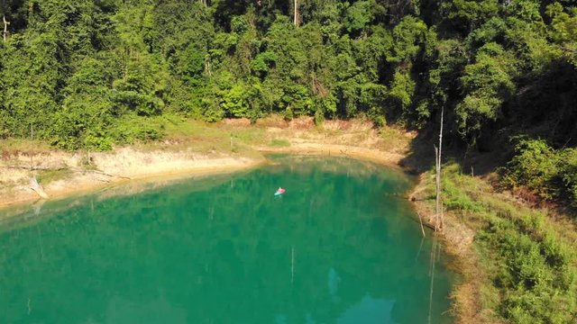 Paddling Across The Beautiful Turquoise Lake Neath The Lush Green Forest Mountain In Thailand - Mavic Drone Shot