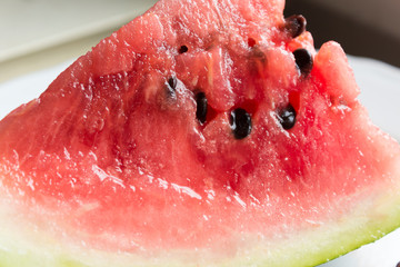 A slice of watermelon on a white plate. Red pulp and black seeds. Close up. Site about summer, fruits and berries, health, cuisine, travel.