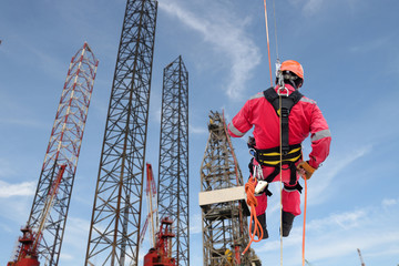 Industrial rope access abseiler welder wearing safety harness, abseiling commencing on structure steel of rig drilling background