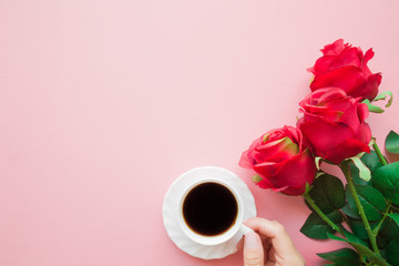 Young woman hand holding white cup of black coffee. Red artificial roses. Empty place for...