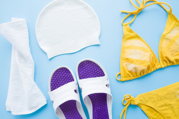 Female accessories for swimming in pool on light blue table background. Pastel color. Closeup. Top down view.