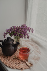 Clay teapot, cup of tea, a bouquet of lilacs on a straw stand.