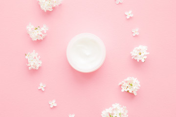 Opened jar of natural herbal cream for women on pastel pink table. Beautiful branches of fresh, white lilac flowers. Care about clean and soft face, hands, legs and body skin. Close up. Flat lay.