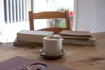 white cup with cappuccino coffee accompanied by a series of books on a rustic wooden table