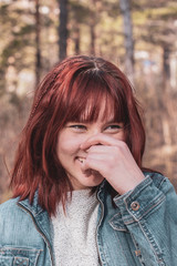 A young girl with red hair laughs and holds her hand to her nose. Looking away. Blurred background. Tinted. Vertical.